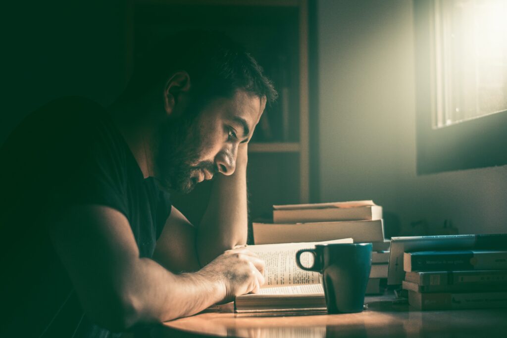 Hombre leyendo un libro junto a una taza de cafe.