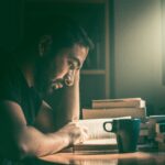 Hombre leyendo un libro junto a una taza de cafe.